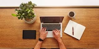 overhead shot of person on keyboard of open laptop with plant notebook ipad and coffee around it